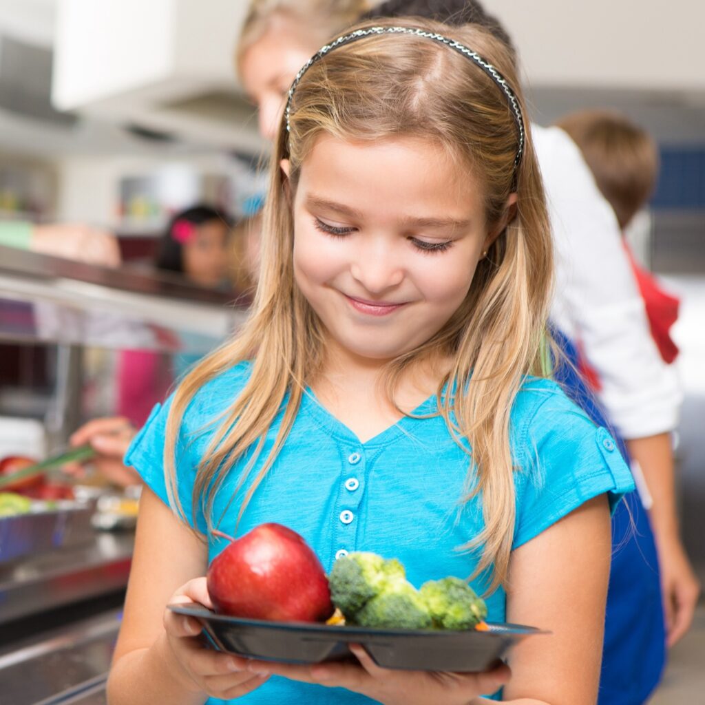 Happy little girl making healthy choices in school cafeteria.